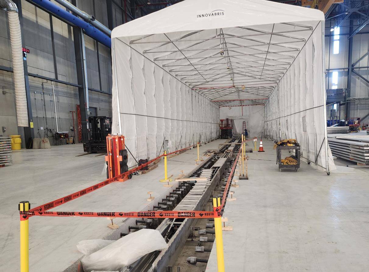 Large white industrial tent with construction materials inside, surrounded by caution tape in a warehouse setting.