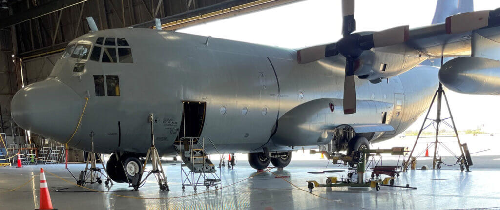 A large military cargo plane undergoes maintenance in a hangar, surrounded by tools and safety cones.