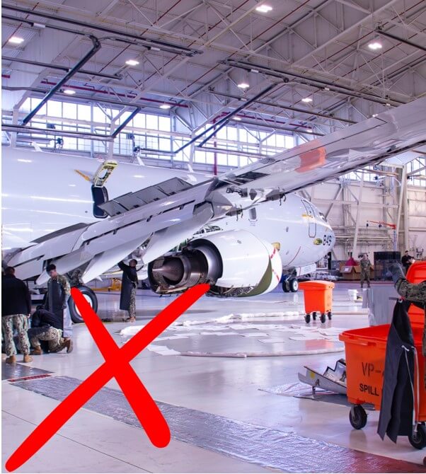 Aircraft maintenance in hangar with red X marker, people work nearby.