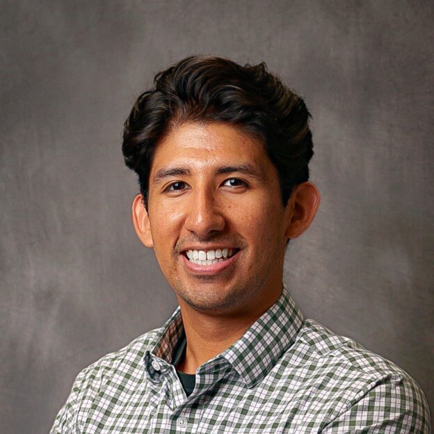 Smiling person in a checkered shirt against a gray backdrop.