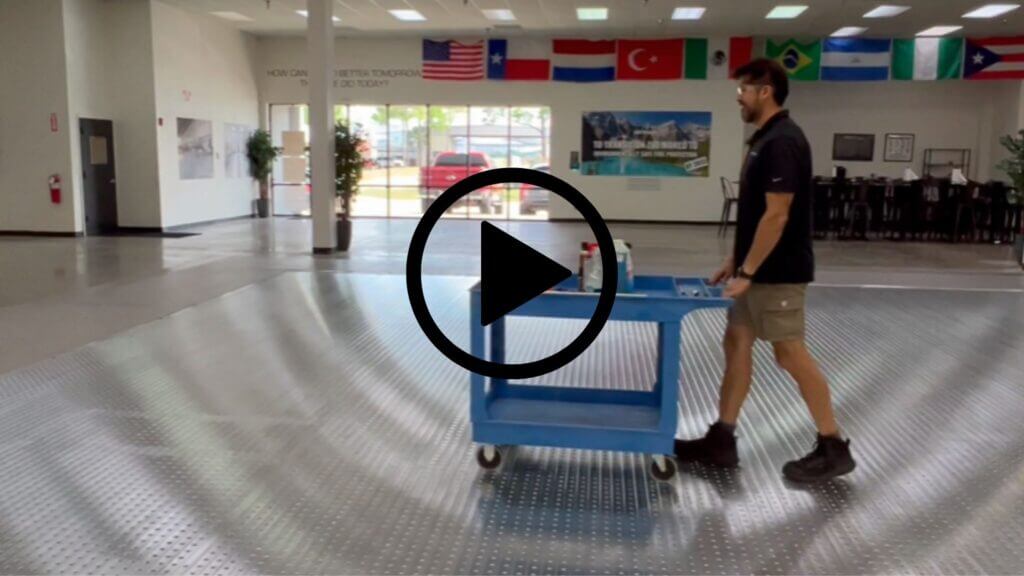 Man pushes blue cart on grooved metal floor in spacious room with flags hanging above.