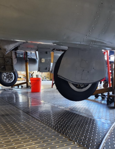 Aircraft landing gear undergoing maintenance in a hangar, surrounded by tools and equipment on a metal floor.