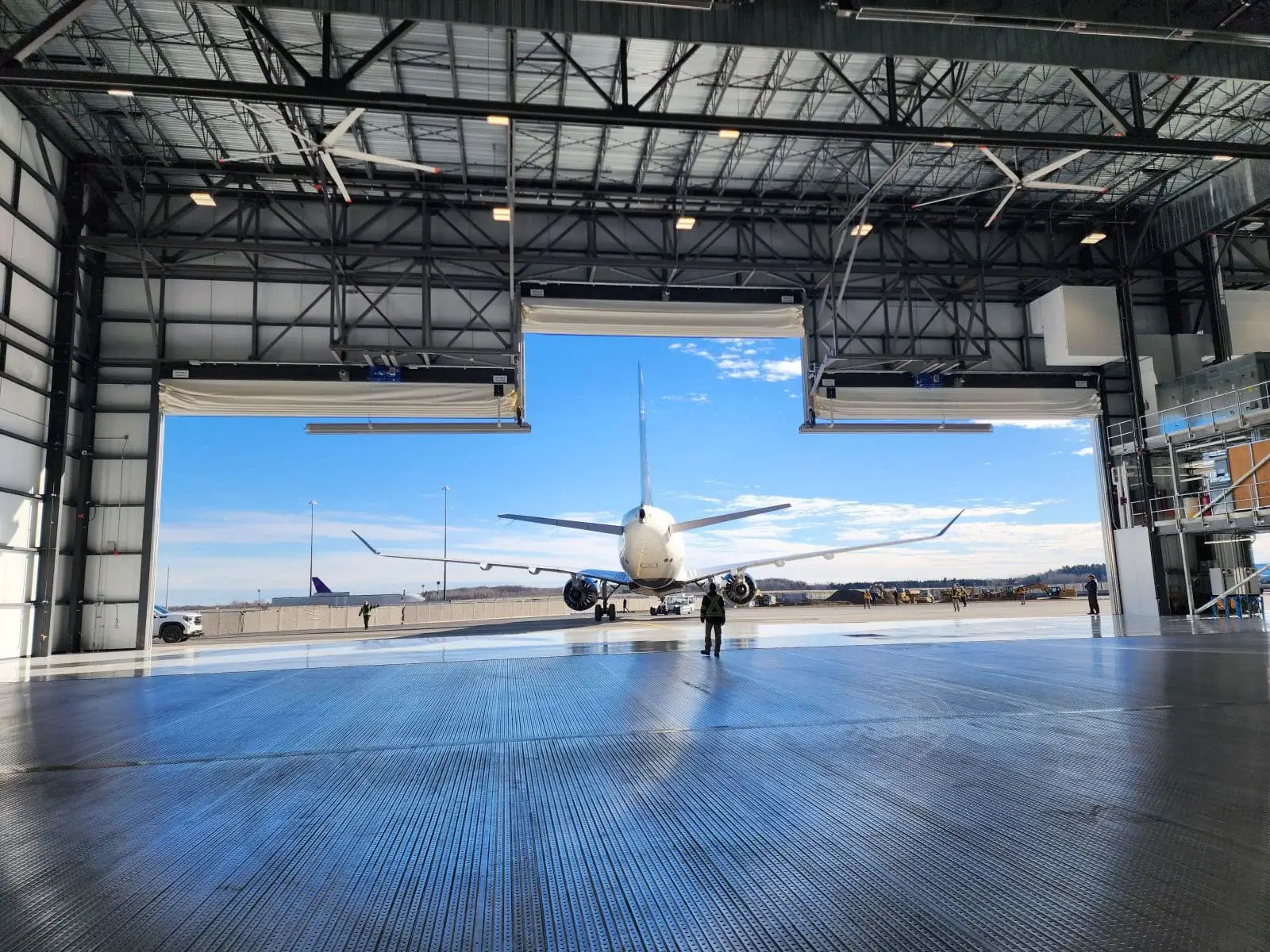 Aircraft taxiing out of a large hangar onto the runway under a clear blue sky.