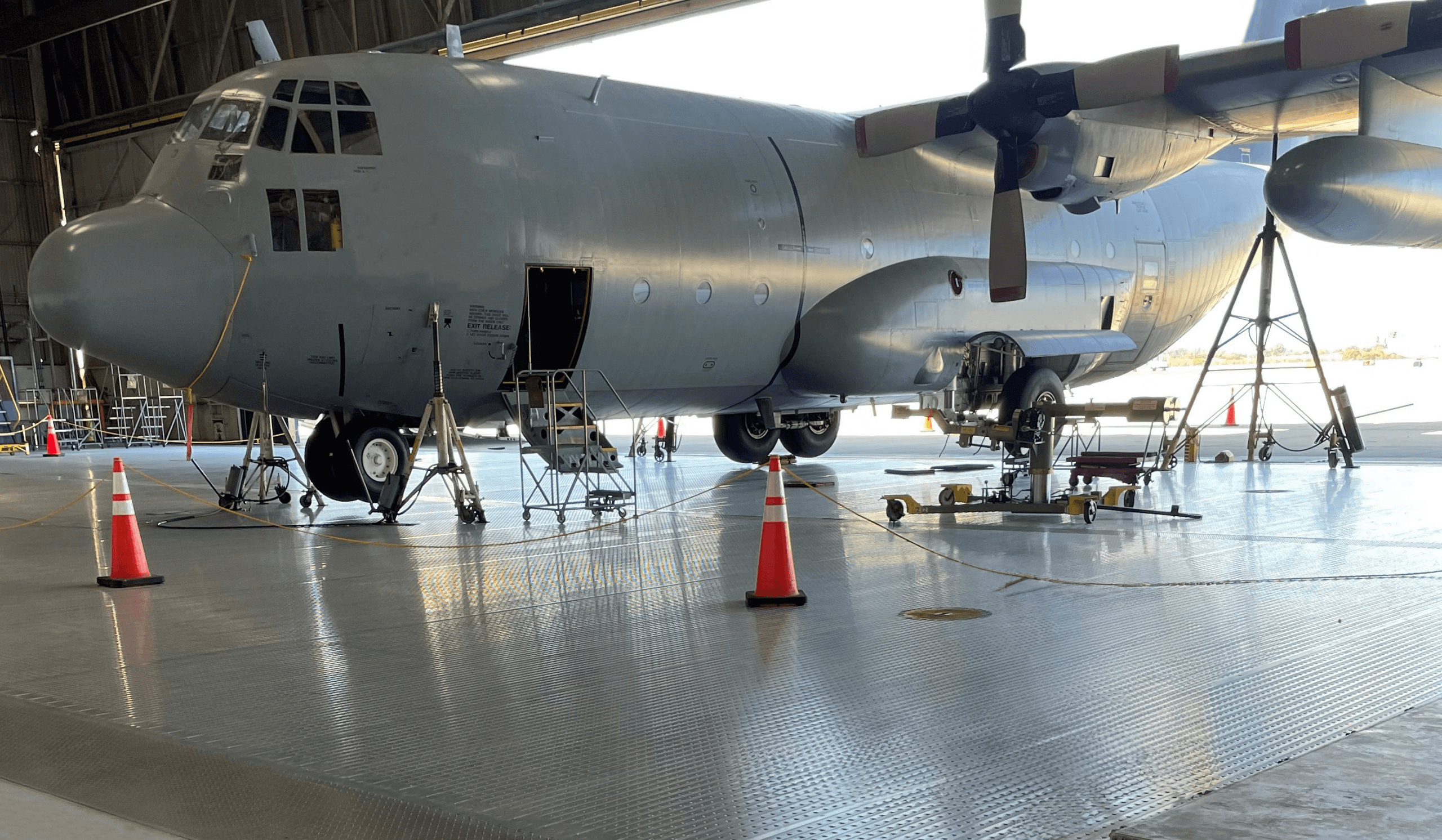 Military cargo plane undergoing maintenance in a hangar, surrounded by safety cones and equipment.