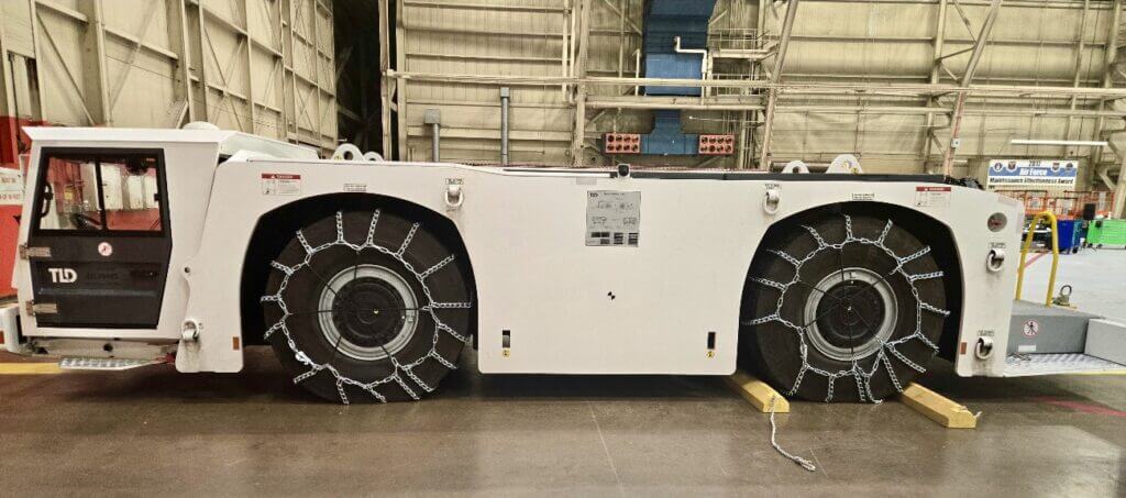 Airport tug with chain-covered wheels parked in a hangar.