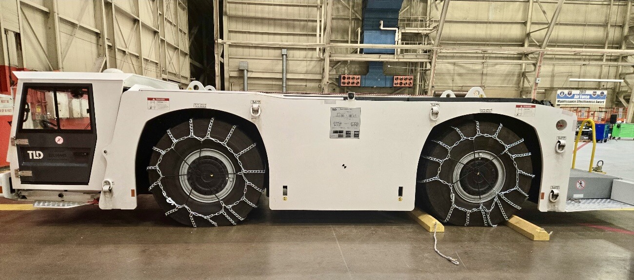 Airport tug with chain-covered wheels parked in a hangar.