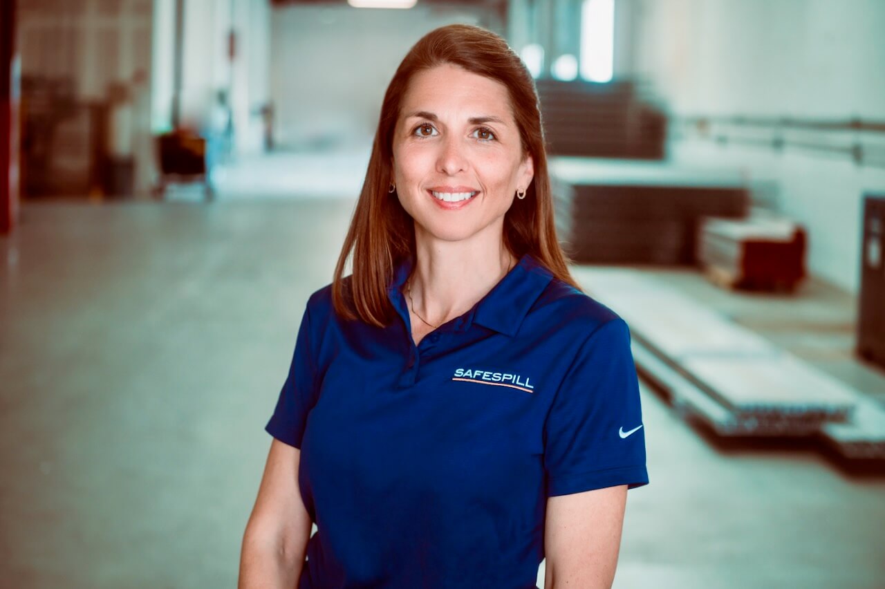 Person in a blue Safespill shirt smiling in an industrial setting.