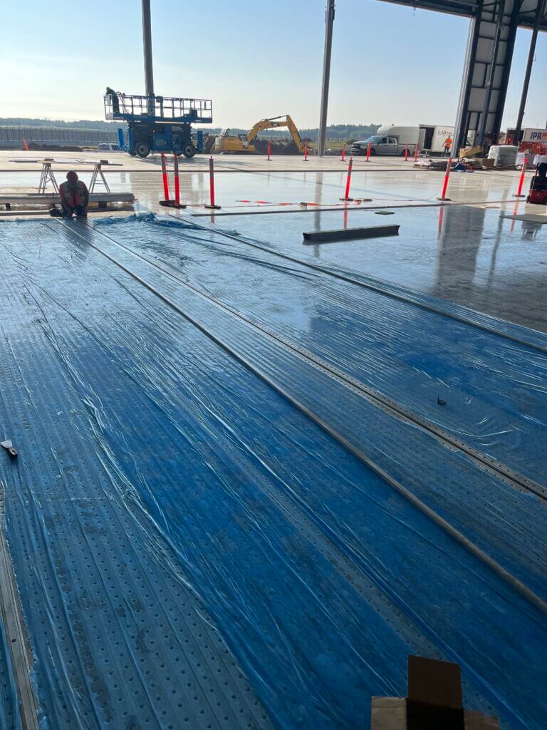 Construction worker installing blue spill containment flooring in a large open warehouse space.