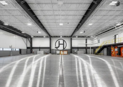 Spacious industrial warehouse interior with high ceiling, metal flooring, and safety equipment in view.