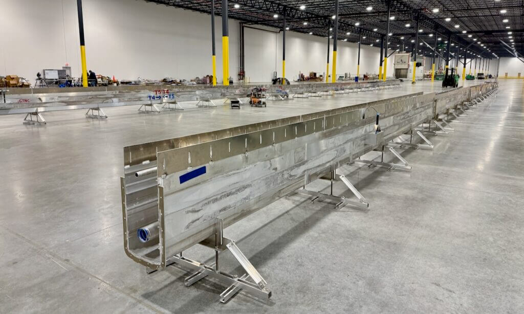 Long metal spill containment barrier in a spacious warehouse setting.