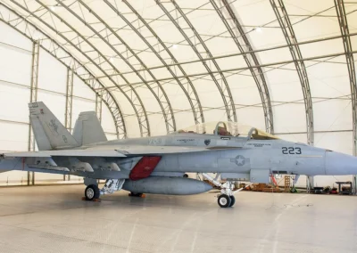 Fighter jet parked inside an aircraft hangar with arched ceiling.