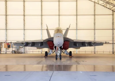 A fighter jet parked in a large hangar with open doors, showing its front view.