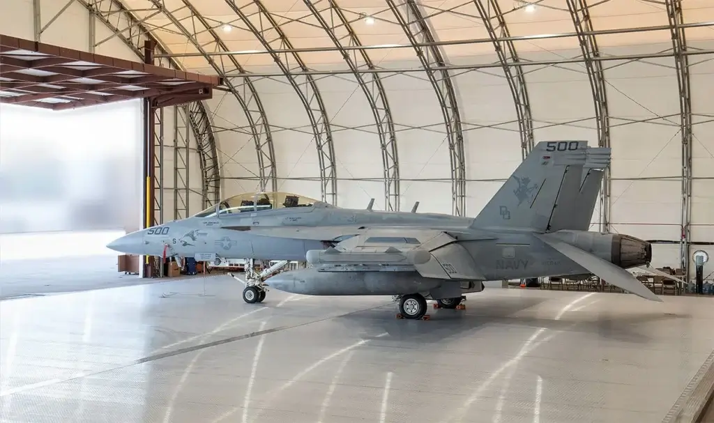 Military jet parked inside a large aircraft hangar, ready for deployment.