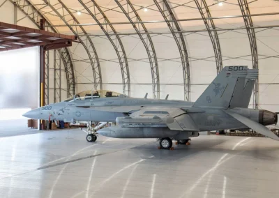 Military jet parked inside a large aircraft hangar, ready for deployment.