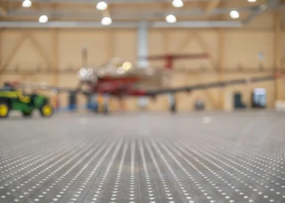 Hangar with blurred plane and vehicle in background, focus on textured metal floor.