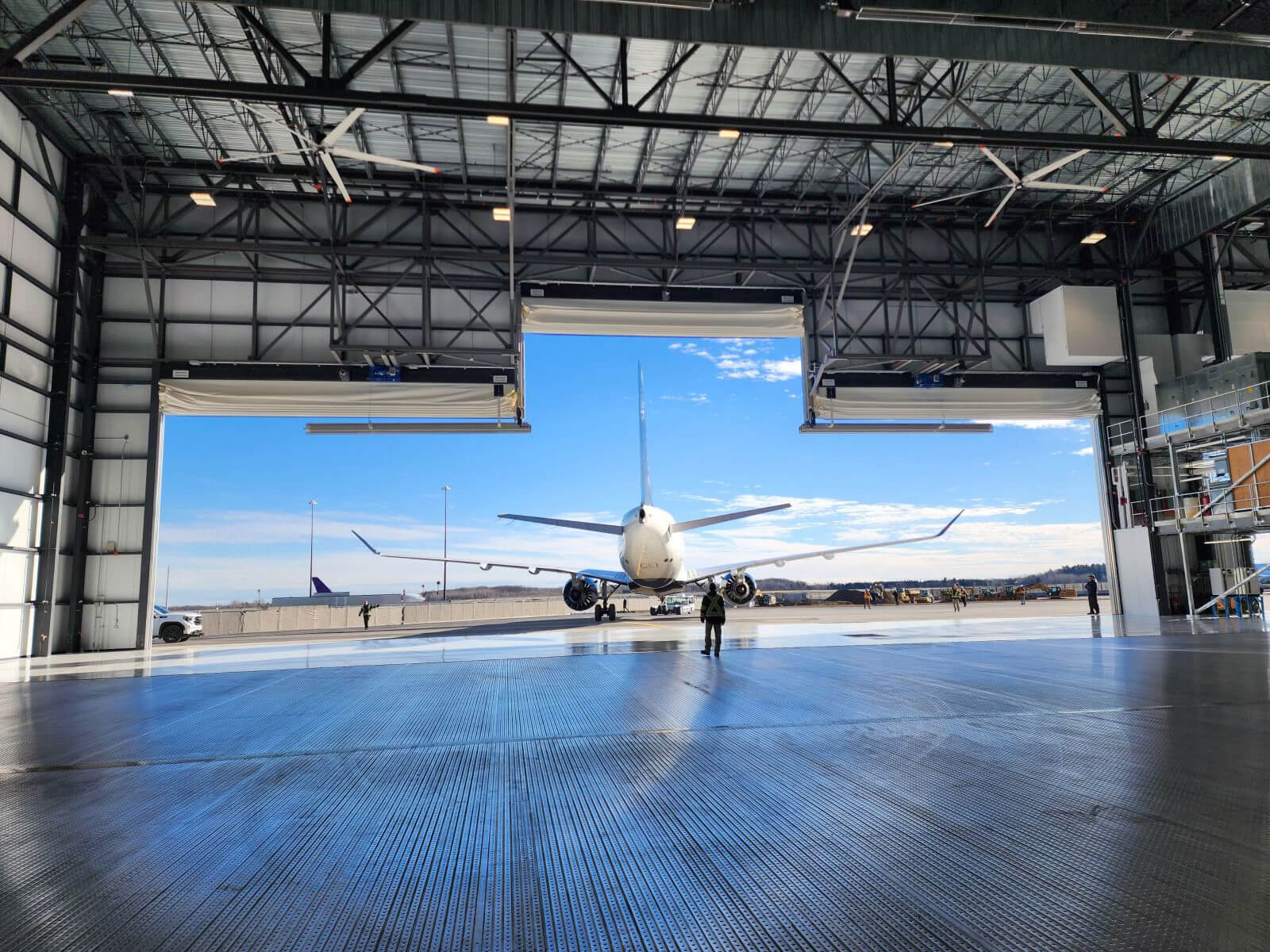 Jet parked in an open hangar under a clear blue sky, with workers nearby.