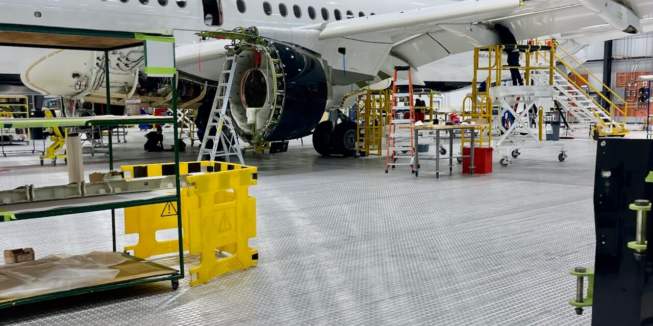 Aircraft undergoing maintenance in hangar with ladders and equipment around it.