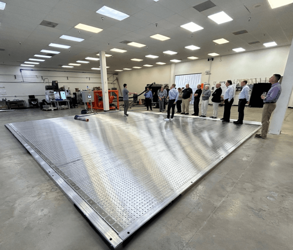 Person demonstrating a spill containment system to a group in a large, well-lit industrial space.