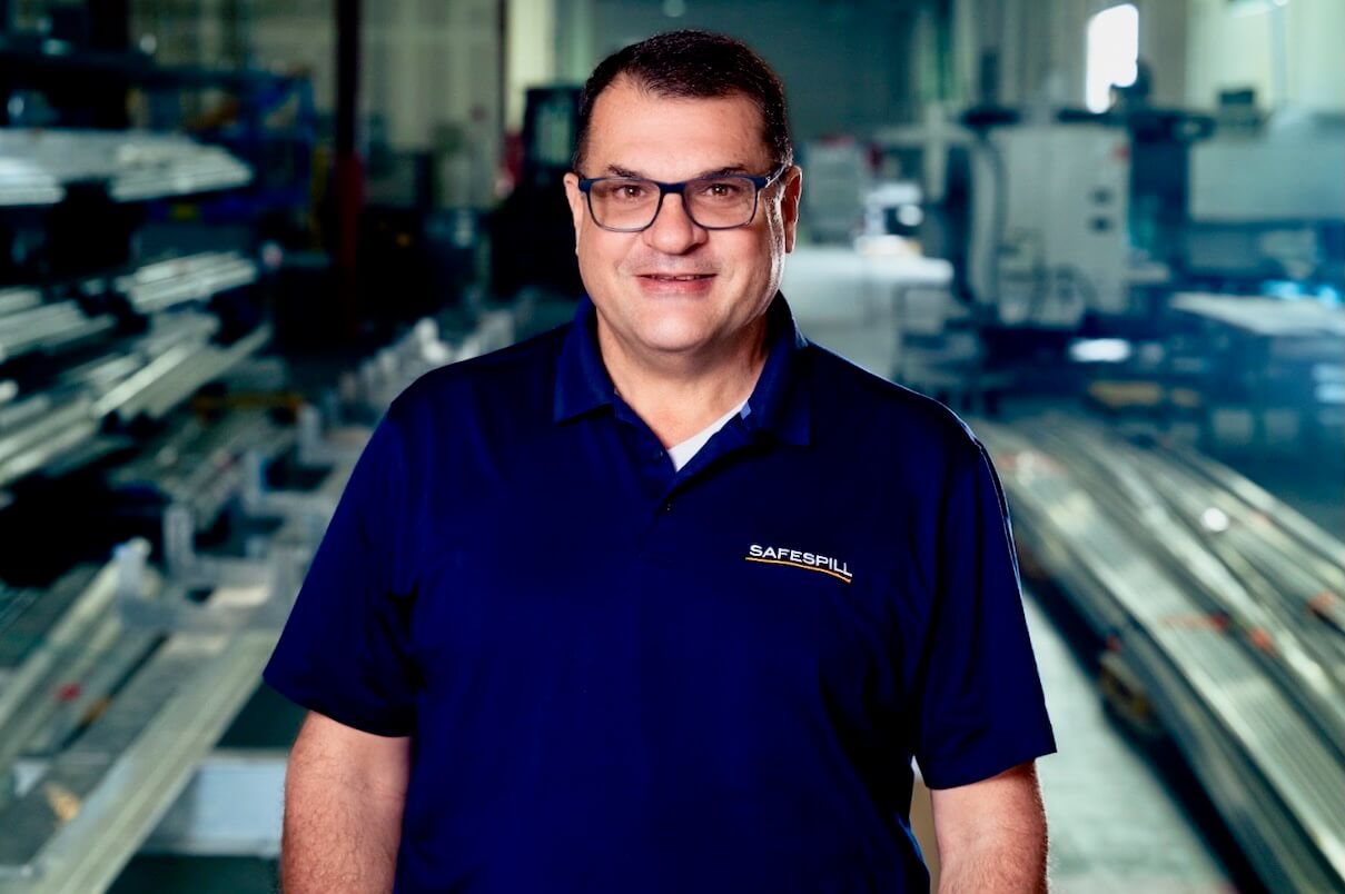 Man in a Safespill shirt smiling in a warehouse setting.