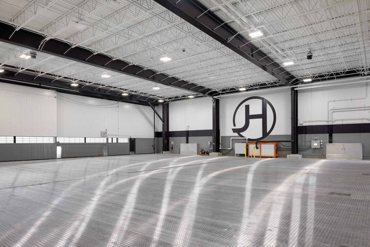 Spacious industrial warehouse with high ceiling, large logo on wall, and metal grid flooring.
