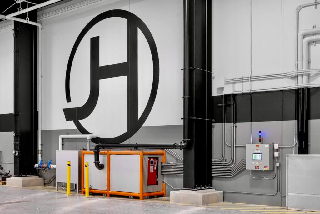 Industrial wall with large logo, pipes, and control panel in a warehouse setting.
